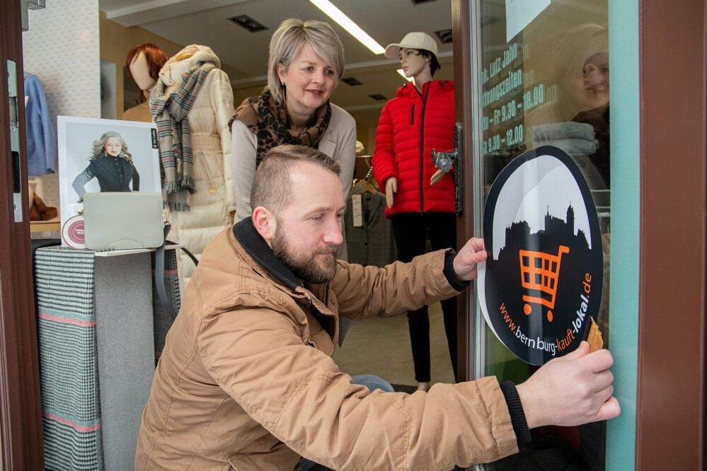 Steffen Hergesell von der Druckbude in Bernburg bringt die neuen Aufkleber an den Schaufenstern in der Innenstadt an. Alle Geschäfte mit diesem Sticker sind auf dem digitalen Marktplatz im Internet vertreten.