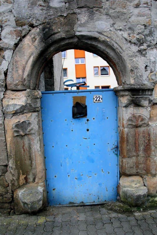 Bilder eines Dorfes: ältestes Portal in Bernsdorf mit profaner Blechtür und Blick auf sanierten Neubaublock.