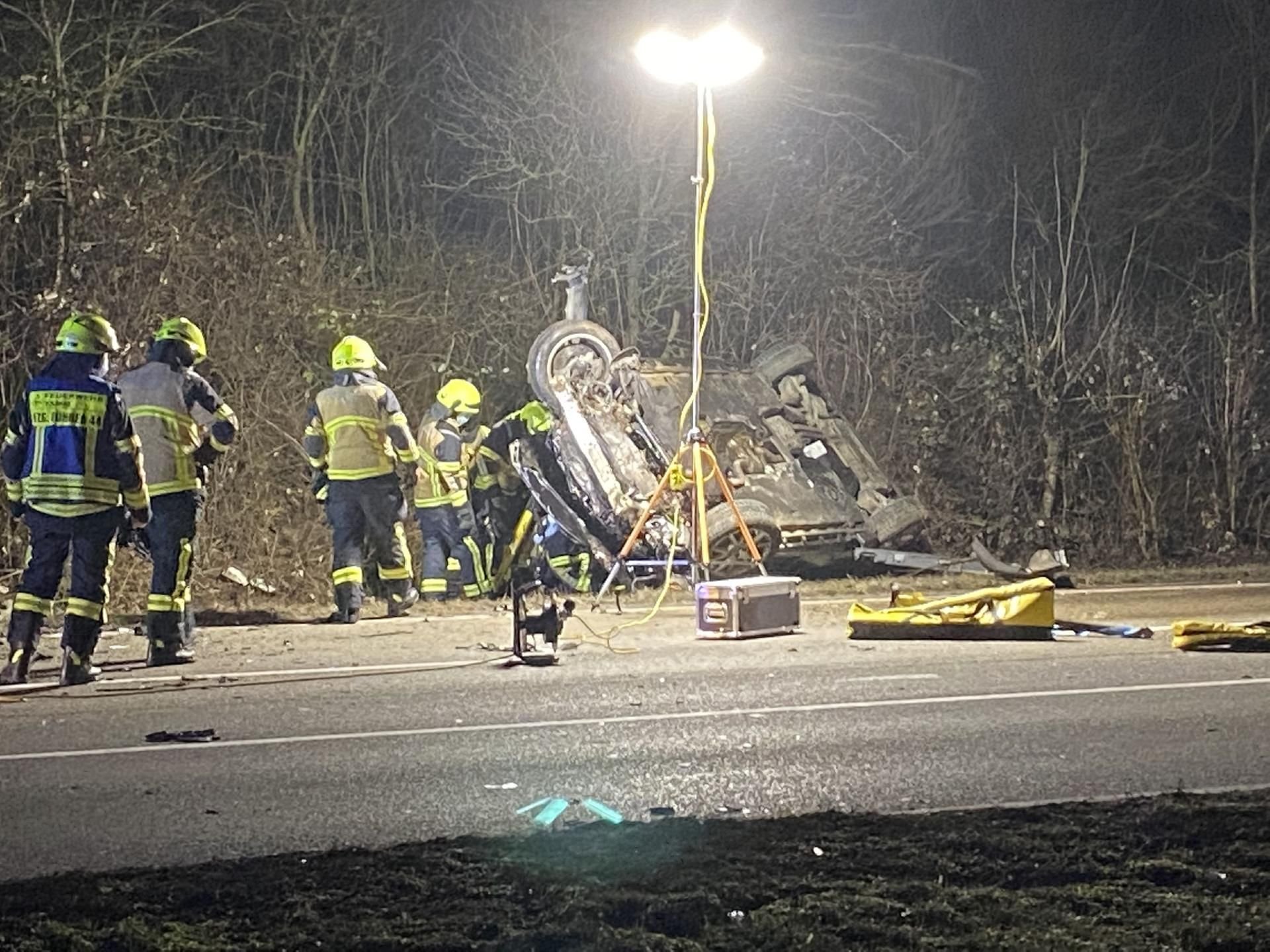 Einsatzkräfte der Feuerwehr stehen bei einem auf dem Dach liegenden Unfallfahrzeug.
