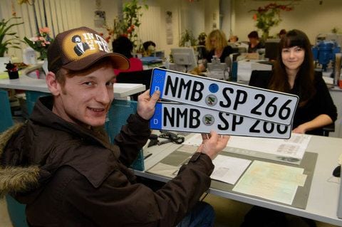 Swen Falkenberg zeigt die NMB-Kennzeichen, auf die Verwaltungsfachangestellte Sophie Goetz soeben die Prägemarken aufgebracht hat.