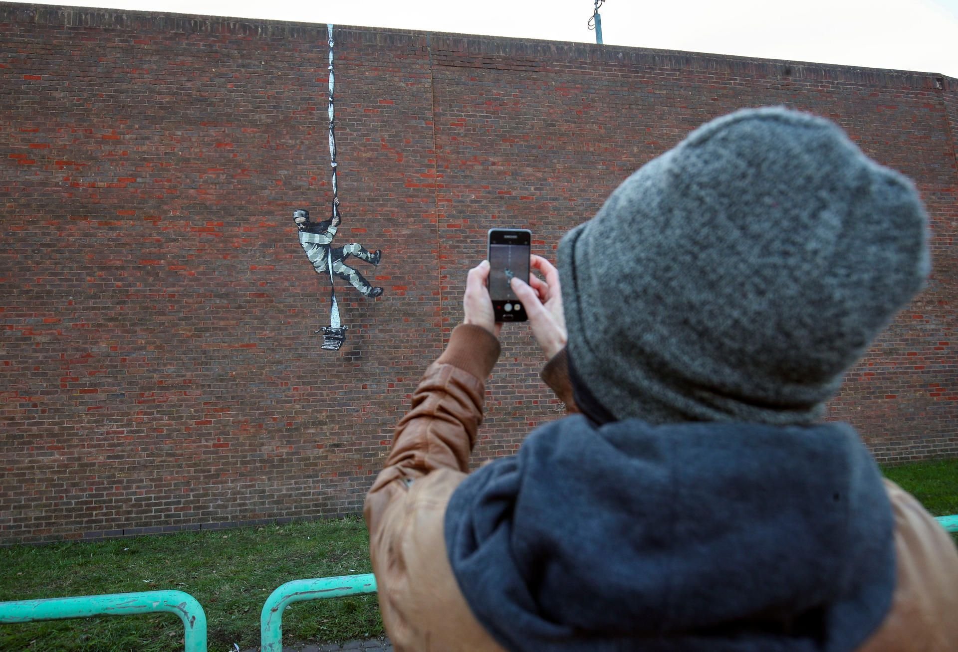 Ein Passant fotografiert ein Bild, das einen ausbrechenden Häftling darstellt. Der Künstler Banksy hat sich dazu bekannt, das Bild an eine Wand eines ehemaligen Gefängnisses gemalt zu haben.