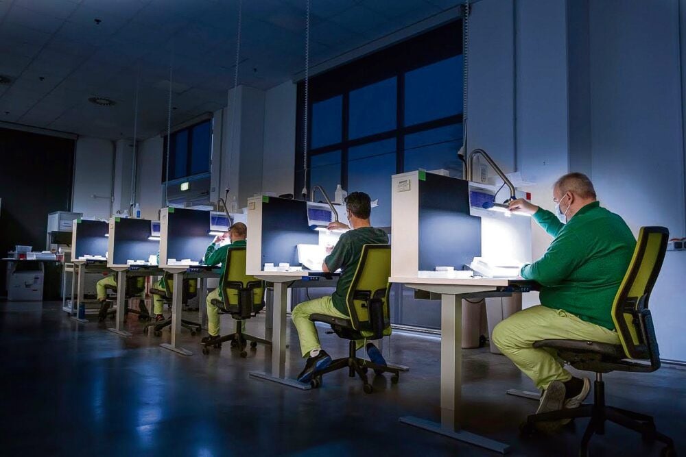 In einem abgedunkelten Raum überprüfen Mitarbeiter des Pharmaunternehmens Mibe jede Impfstoff-Ampulle einzeln auf Einschlüsse oder Glassplitter. Erst dann darf das Serum versendet werden.