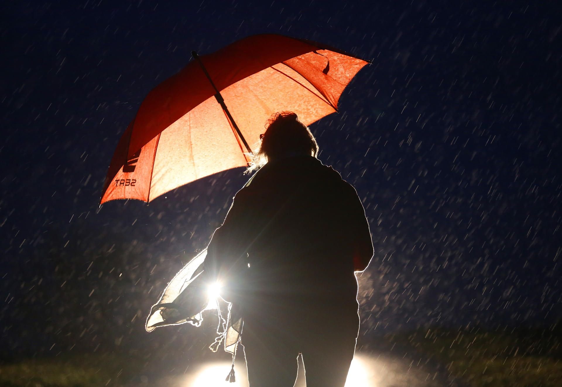 Illustration: Eine Frau ist am frühen Morgen bei Regen mit Regenschirm auf dem Weg zu ihrer Arbeit. Selbst im Flachland gab es im Norden Orkanböen über 120 km/h.