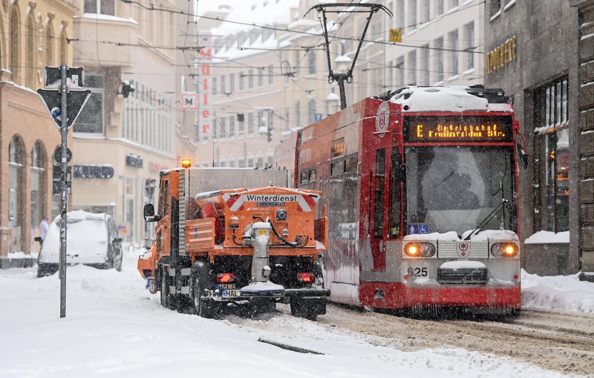 Eine Straßenbahn steht neben einem Räumfahrzeug in der Altstadt von Halle.