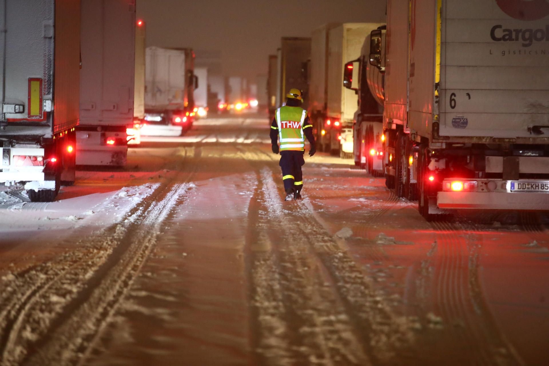 Mitarbieter des Technischen Hilfswerks (THW) betreuen Lkw-Fahrer, die auf einer verschneiten Autobahn im Stau stehen.