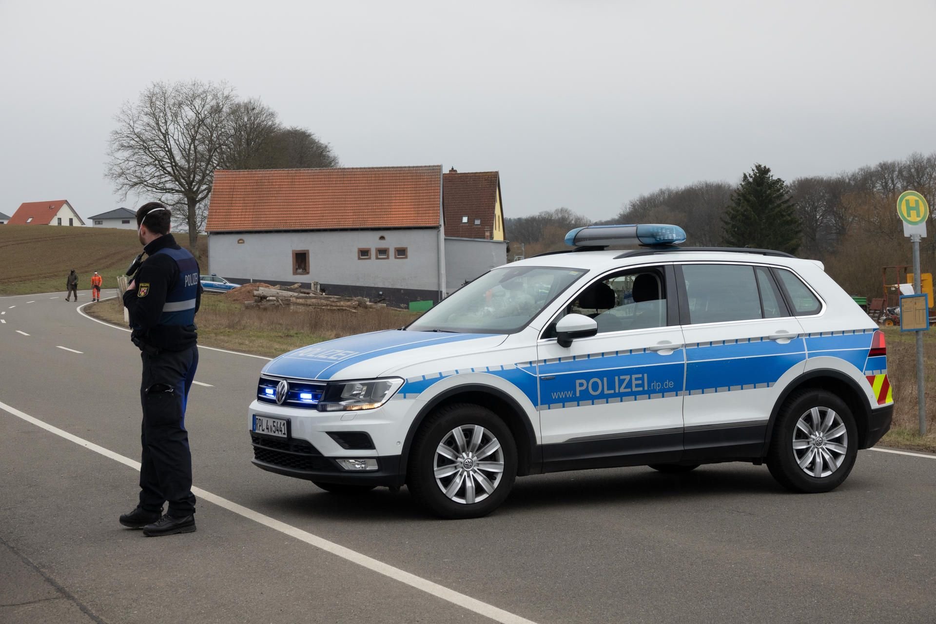 Ein Polizist mit Einsatzfahrzeug sperrt eine Straße nachdem in einem Wohnhaus in Weilerbach bei Kaiserslautern zwei Leichen entdeckt worden waren.