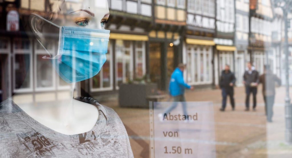 Eine Schaufensterpuppe mit einer medizinischen Maske steht in einem geschlossenen Modegeschäfts, während sich die Einkaufsstraße und Fachwerkhäuser im Schaufenster spiegeln. Aufgrund des Lockdowns sind Geschäfte noch immer geschlossen. +++ dpa-Bildfunk +++