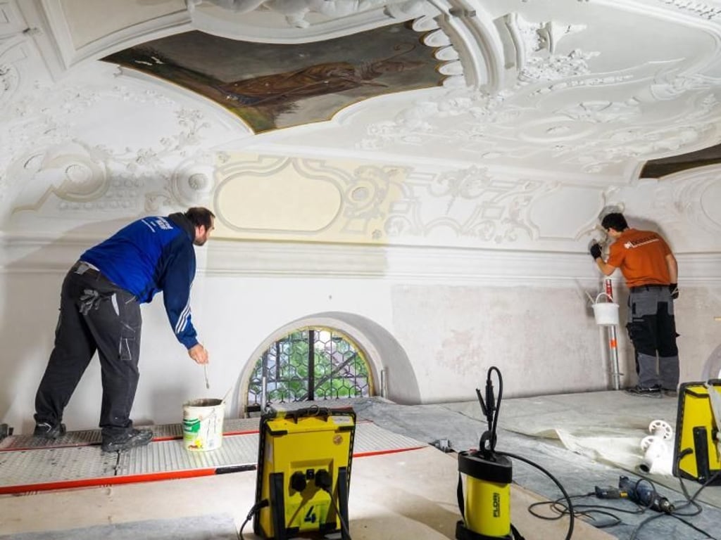 Statt Gelb und Grau wieder ein strahlendes Weiß: Philipp Dörfler (r) und sein Kollege Christian Müller restaurieren die Pfarrkirche St. Vitus in Hirschaid (Bayern). Foto: Nicolas Armer/dpa-tmn