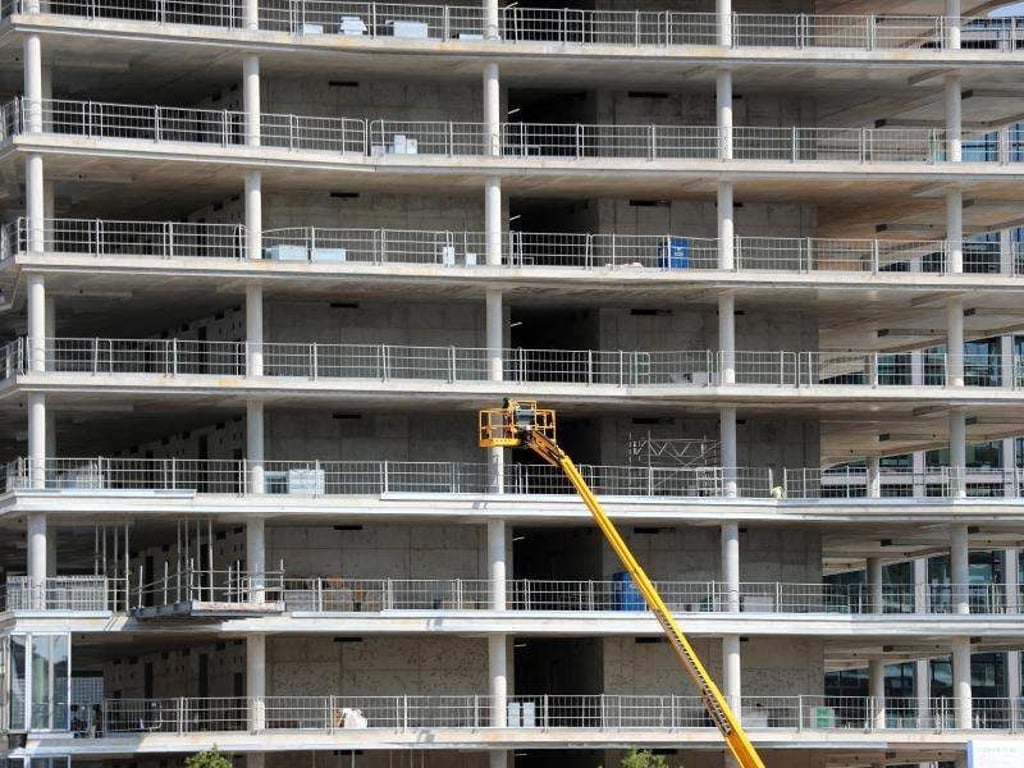 Arbeiter montieren von einer Hebebühne aus Teile an einem Neubau. Foto: Jens Büttner/Archiv