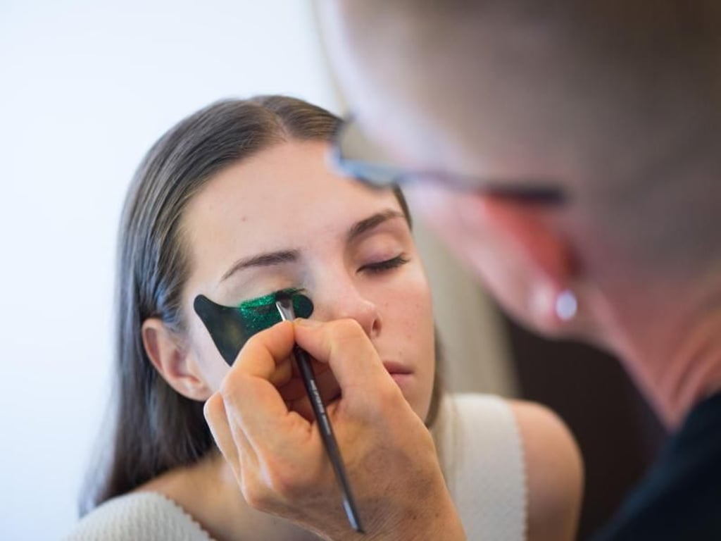 Visagist und Friseurmeister Peter Arnheim aus Berlin schminkt das Oberlid des Models mit einem breiten glitzernden Eyeliner in Grün. Foto: Klaus-Dietmar Gabbert