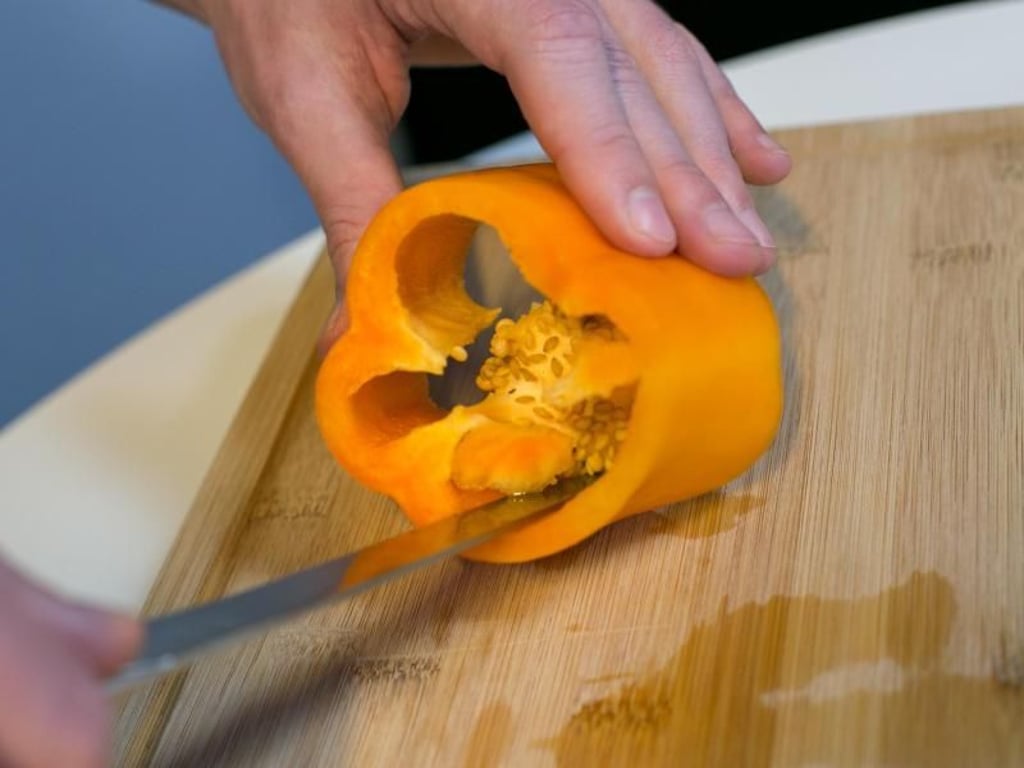 Schritt 3: Die Paprika mit einer Hand leicht schräg halten. Mit dem Messer in der anderen Hand das Kerngehäuse rundherum herausschneiden. Foto: Karolin Krämer