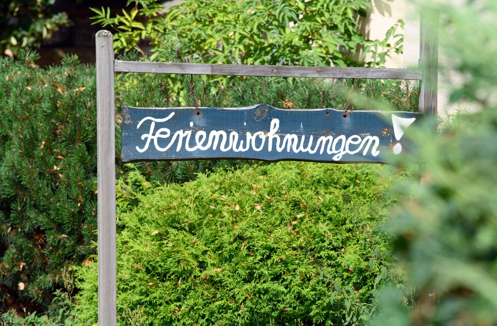 Ein Schild „Ferienwohnungen!“ steht vor einem Haus zwischen Bäumen und Sträuchern. Die Bundesländer haben ein Beherbergungsverbot für Urlauber aus inländischen Corona-Risikogebieten beschlossen. +++ dpa-Bildfunk +++