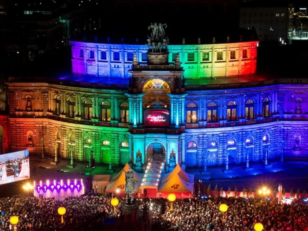Besucher nehmen vor dem farbenfroh angestrahltem Opernhaus an dem Ball teil. Der 11. Semperopernball findet unter dem Motto «Dresden schillert - Der Ball ist bunt» statt. Foto: Arno Burgi