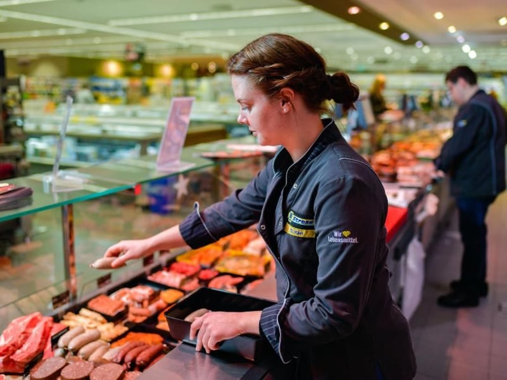 Die Frühschicht beginnt damit, dass die Verkaufstheke aufgefüllt wird: Diana Kari sorgt im Lebensmittelhandwerk dafür, dass es den Kunden an der Fleischtheke im Edekamarkt Strese an nichts fehlt. Foto: Uwe Anspach