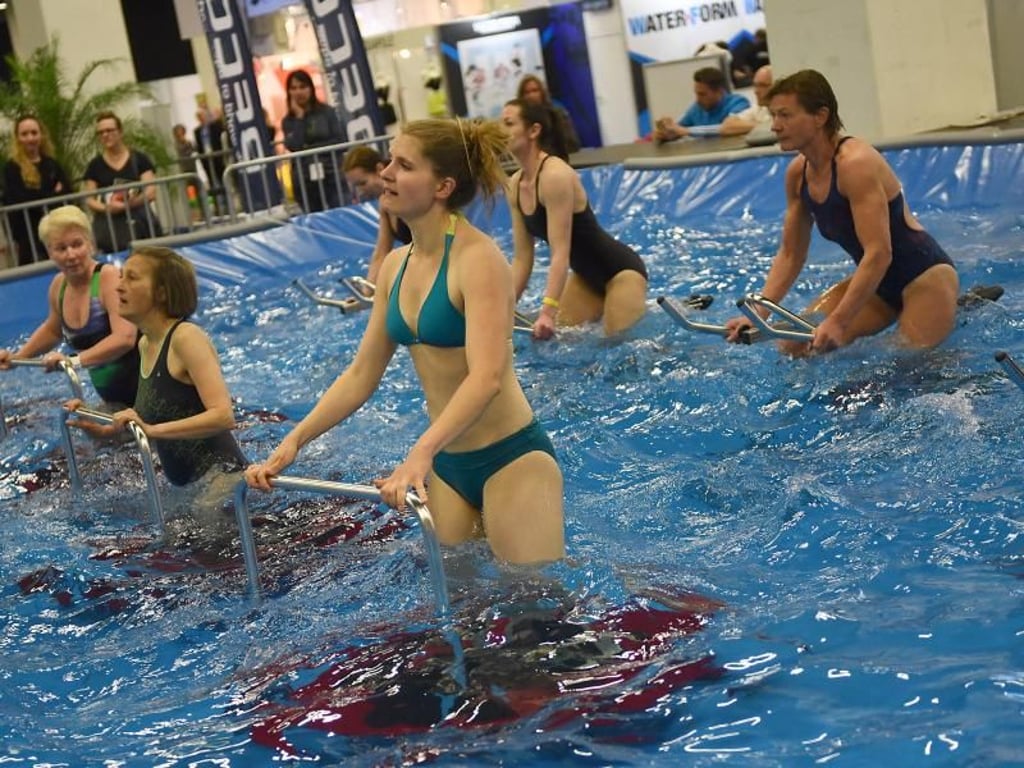 Vorn wird gehüpft, weiter hinten geradelt: Beim High Intensity Interval Training (H.I.I.T) im Pool wechseln sich die Teilnehmer auf dem Trampolin und dem Fahrradergometer ab. Foto: Henning Kaiser/dpa-tmn