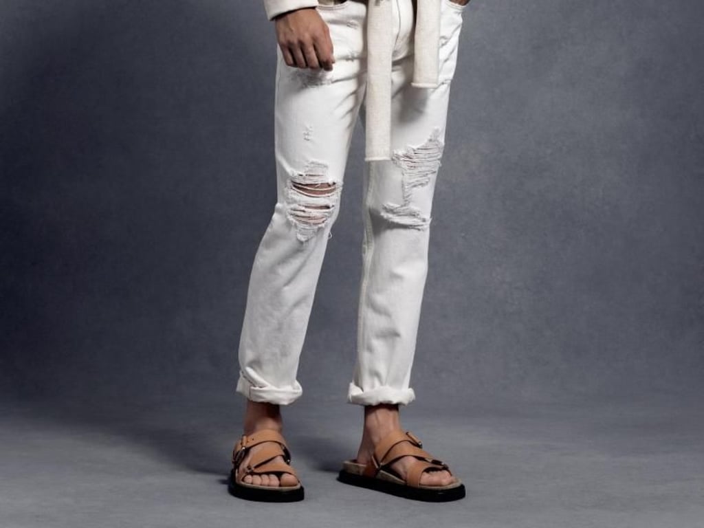 Michael Kors zeigt weiße Destroyed Jeans zu Sandalen - im Sommer dürfen Männer gerne wild kombinieren (Lederjacke 1150 Euro, Pullover 260 Euro, Schal 170 Euro, Jeans 170 Euro, Sandalen 200 Euro). Foto: Michael Kors