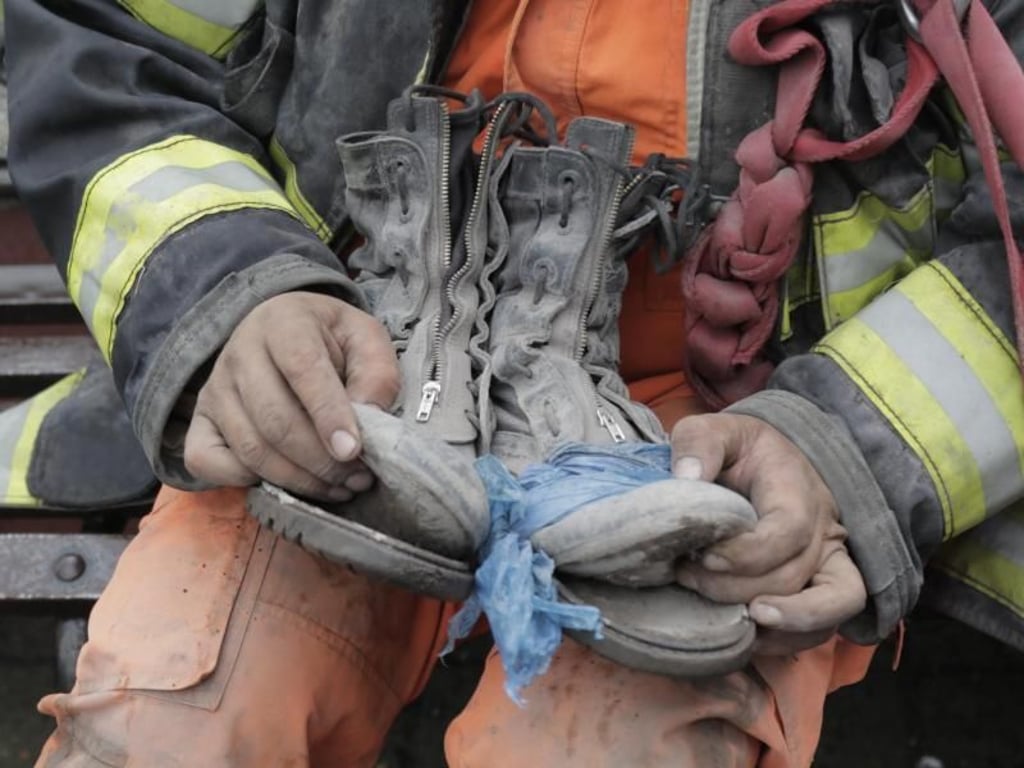 Ein Feuerwehrmann zeigt seine Schuhe, die sich während des Einsatzes am Vulkan auflösen. Foto: Alejandro Balan