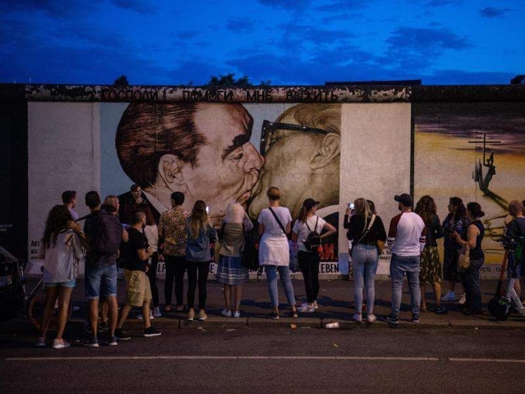 Touristen und Besucher stehen vor dem sogenannten «Bruderkussgemälde» an der East Side Gallery. Vor fast 30 Jahren hatten sich hier Künstler verewigt und das längste noch erhaltene Teilstück der Berliner Mauer mit ihren Kunstwerken umgedeutet. Foto: Arne Immanuel Bänsch