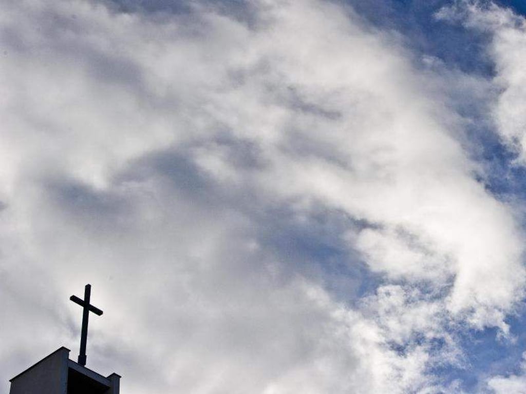 Das Kreuz einer Kirche ist vor bewölktem Himmel zu sehen. Foto: Nicolas Armer/Archiv