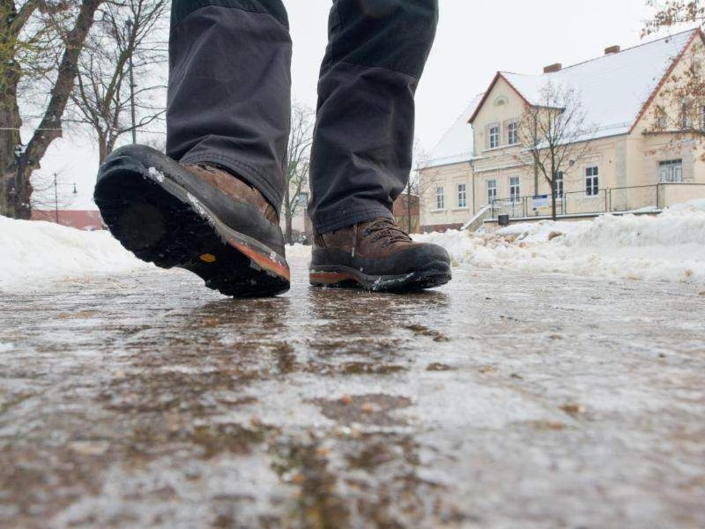 Ein Mann geht auf einem vereisten Gehweg eine Straße entlang. Foto: Patrick Pleul/Archiv