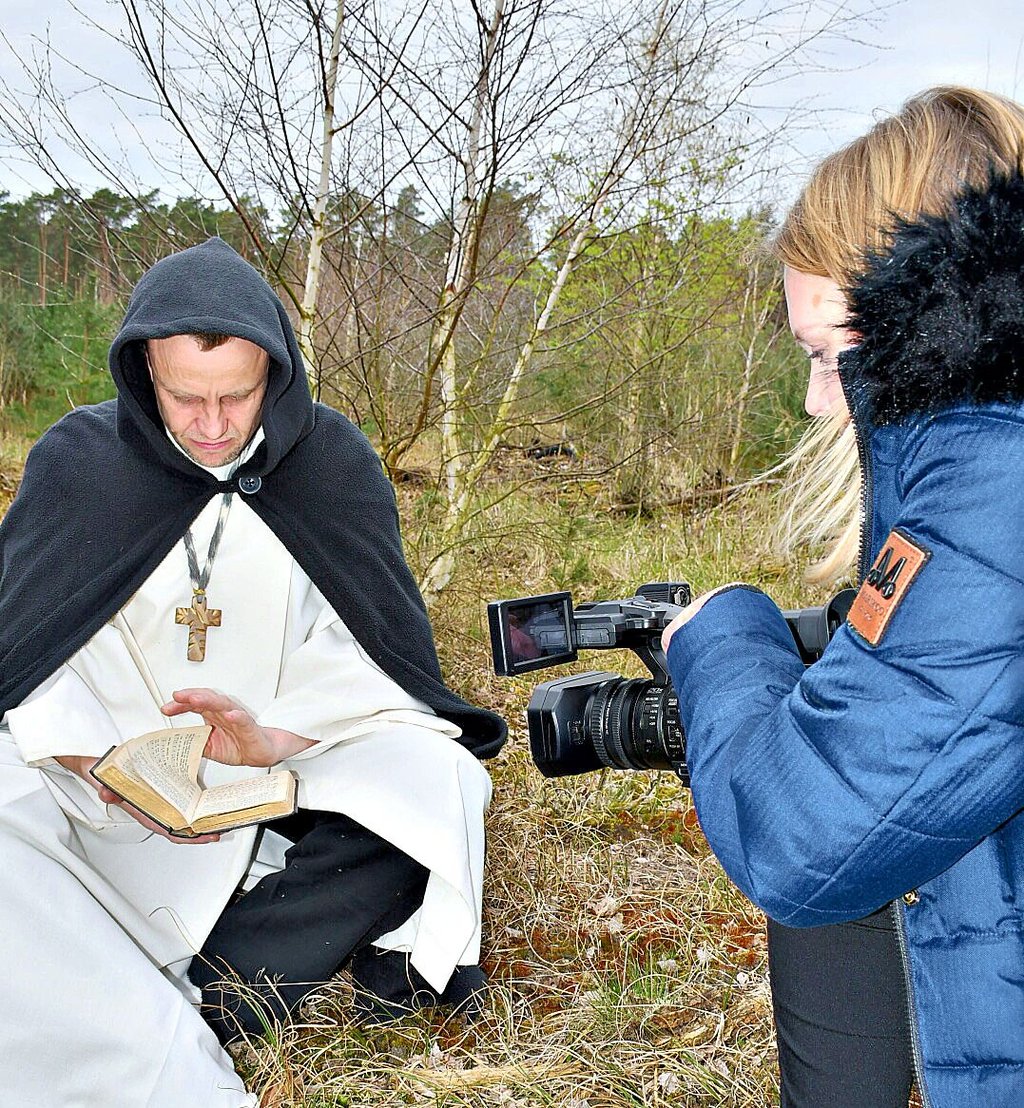 Bruder Norbert von Xanten (Thomas Pelloth) sitzt in der Bibel lesend auf einem Baumstumpf.