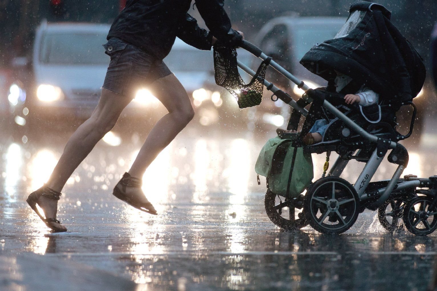 Eine Frau mit Kinderwagen rennt durch einen Regenschauer.