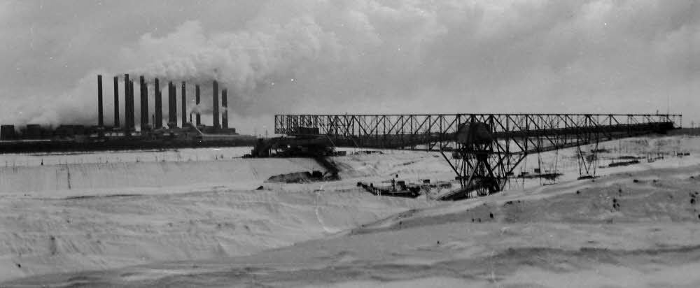 Auf dem Panoramafoto sieht man das Kraftwerk Zschornewitz mit der alten Abraumförderbrücke Golpa. Diese Aufnahme stammt aus dem Jahr 1937. Auch damals bedeutet der Winter eine große Herausforderung nicht nur für die Kumpels.