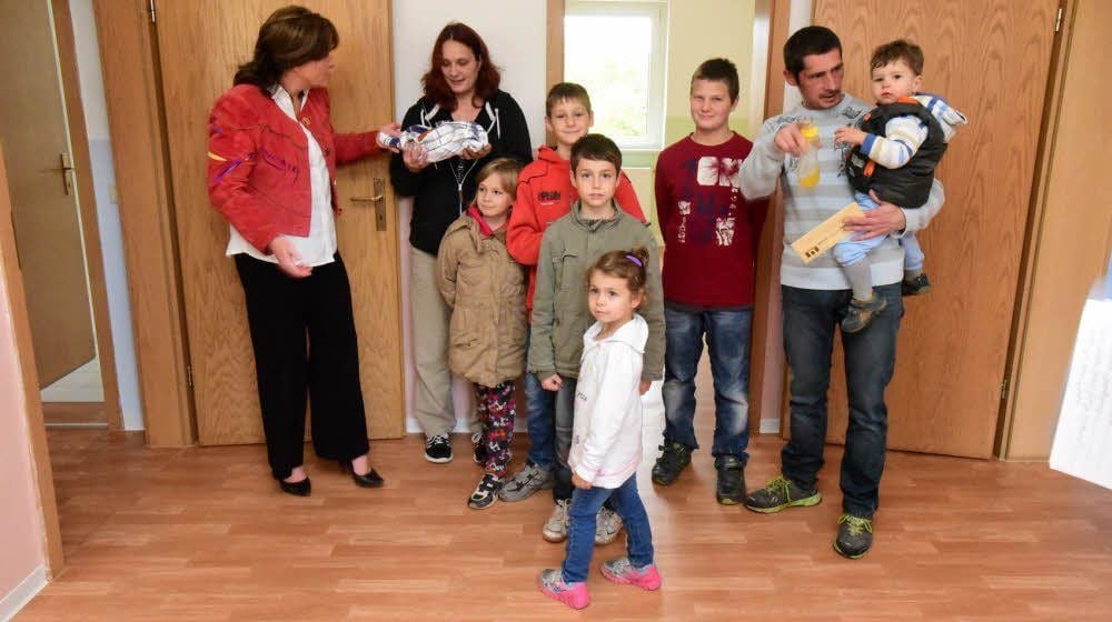 Die Großfamilie nach der Schlüsselübergabe in ihren neuen vier Wänden. WVW-Geschäftsführerin Kathleen Schechowiak (links) überreicht an Mutter Marika Haase einen Laib Brot mit einem Salznäpfchen darin.