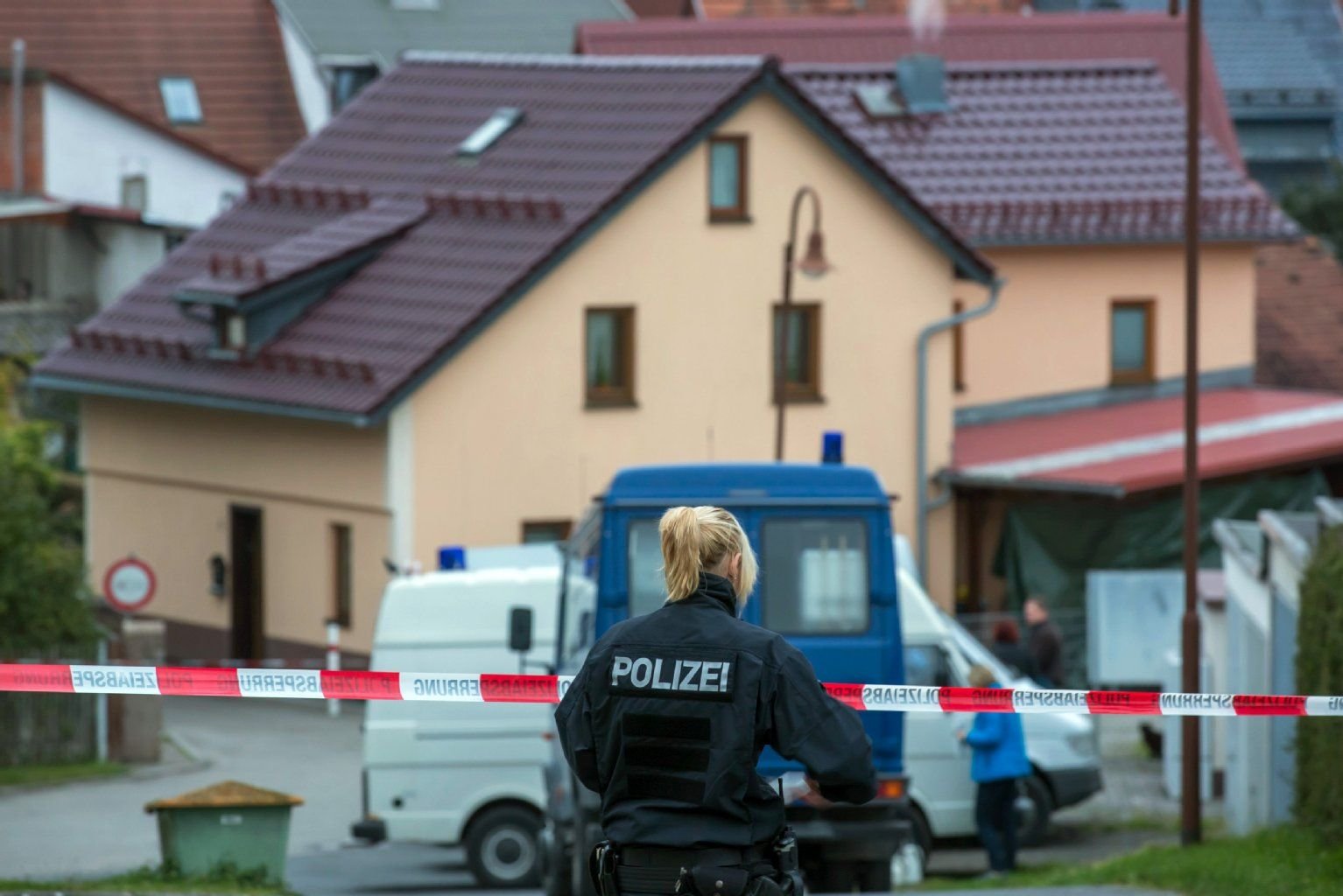 Eine Polizistin steht am 27.10.2014 in Schwarza (Thüringen) vor einem Absperrband um ein Einfamilienhaus, in dem zuvor drei Leichen gefunden worden.