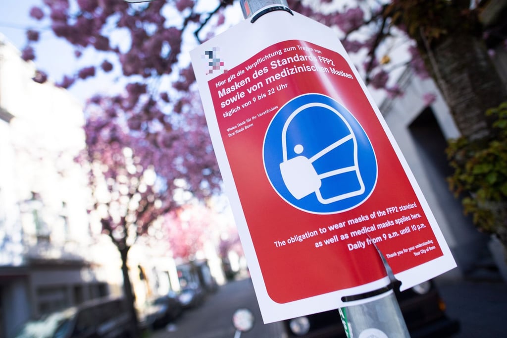 Auf das Tragen einer Maske weißt ein Schild vor den blühenden Kirschbäumen hin.
