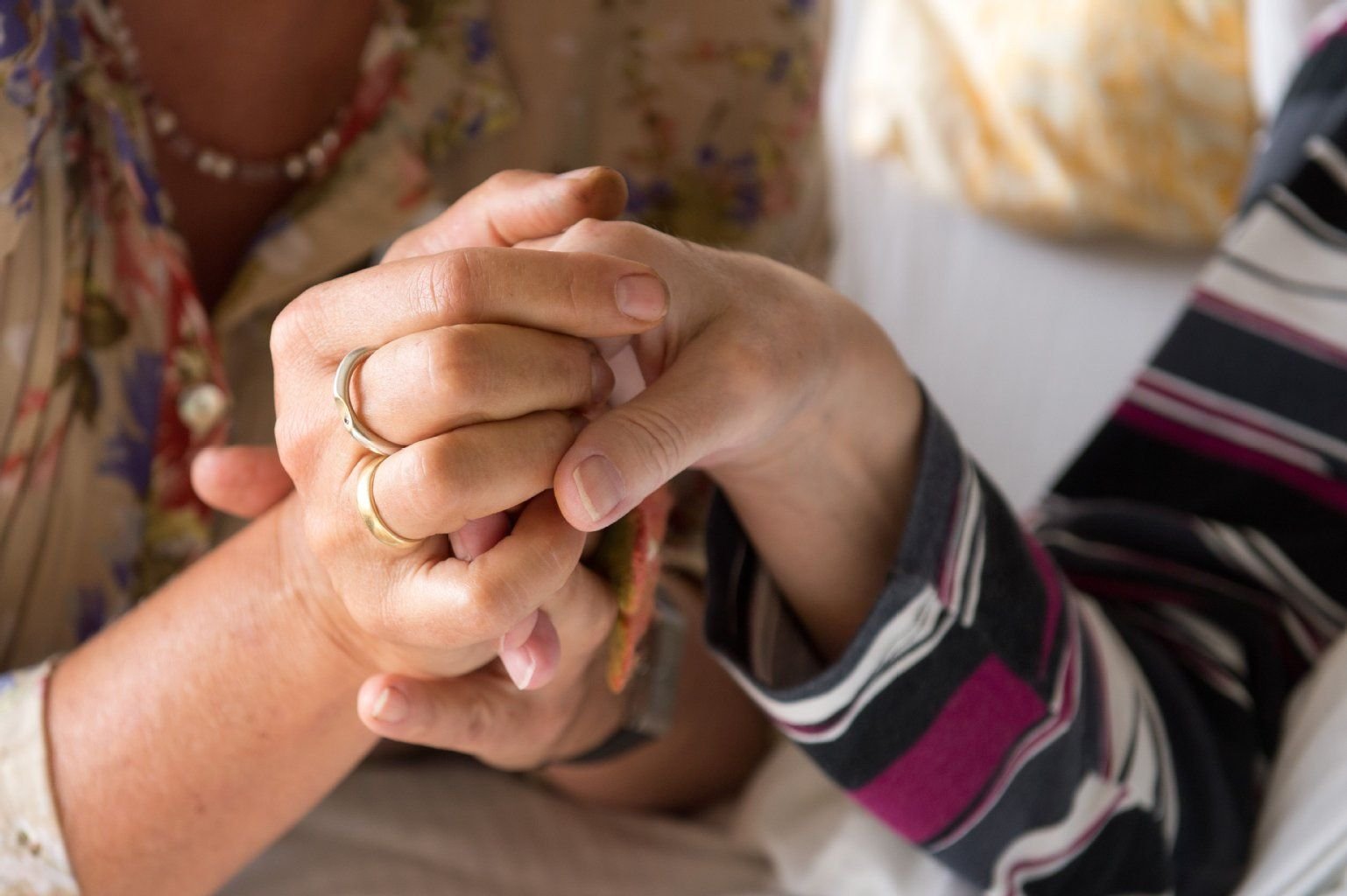 Eine Therapeutin (l) hält in einem Hospiz die Hand einer todkranken Bewohnerin.