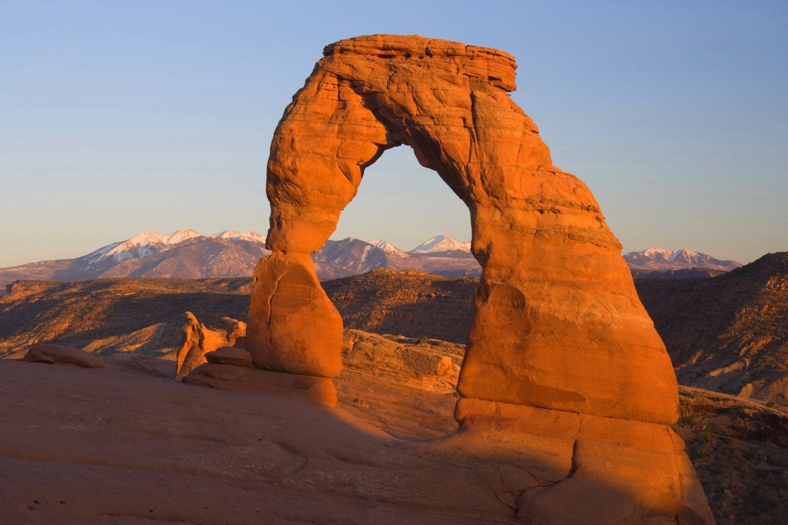 Der „Delicate Arch“, ein fein skulpturierter Felsbogen aus Sandstein, im Arches National Park in Utah, USA. Im Hintergrund: die schneebedeckten Manti-La-Sal-Berge.