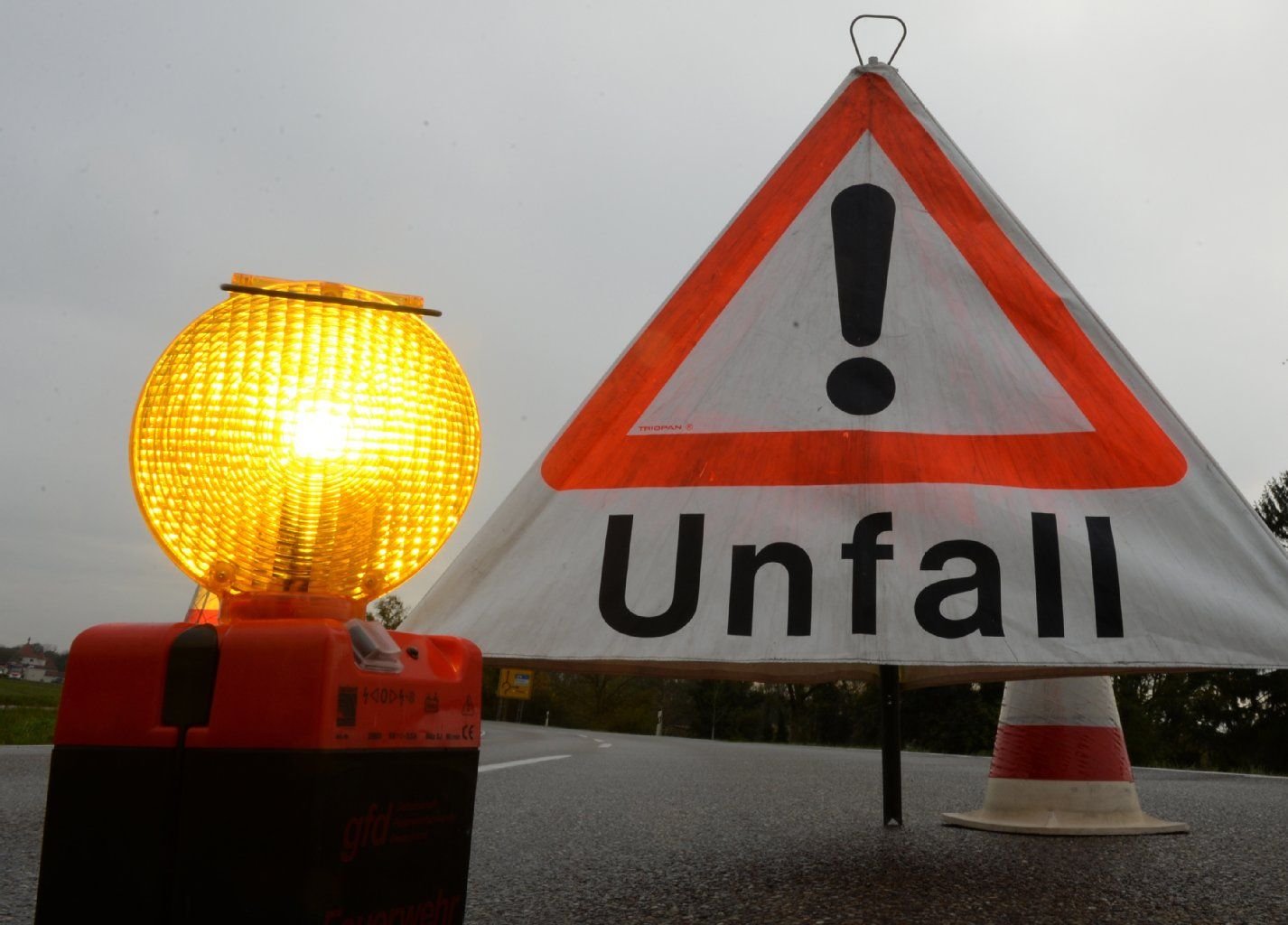 Ein Warnlicht und ein Warndreieck mit der Aufschrift "Unfall" stehen auf einer Fahrbahn.