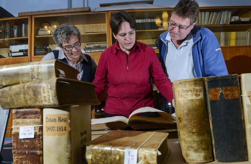 Nicola Hedemann (M.) blättert mit Manuela und Peter Graul aus Bad Frankenhausen in alten Kirchenbüchern.