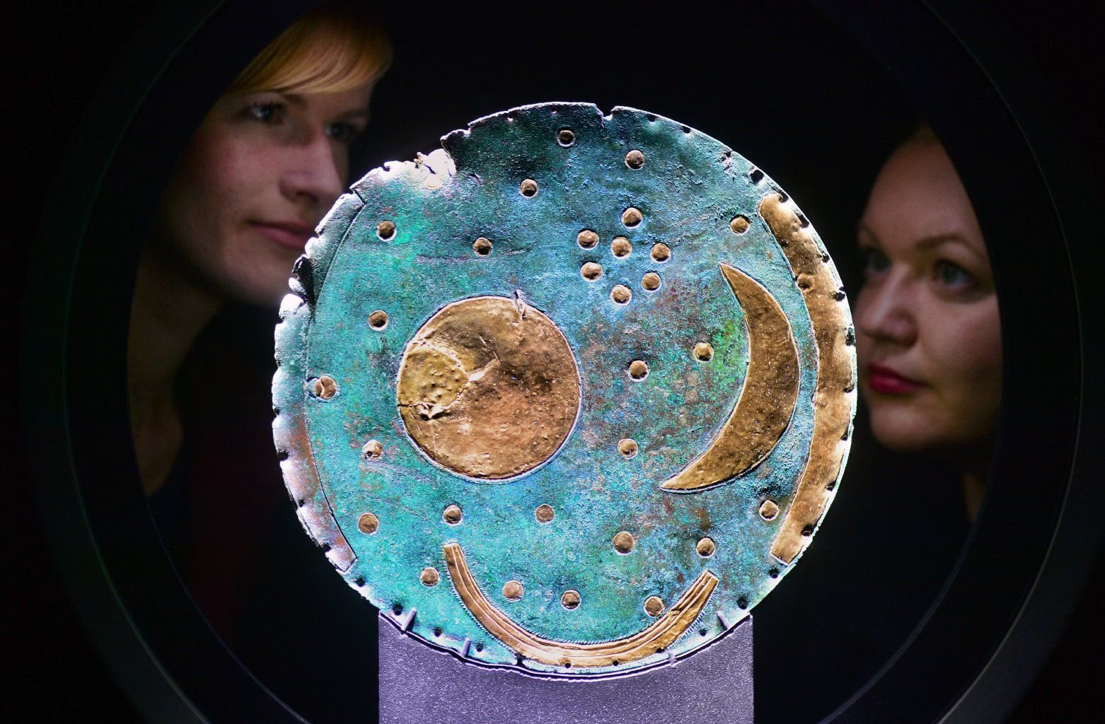 Zwei junge Frauen nehmen im Landesmuseum für Vorgeschichte in Halle (Saale) die Himmelsscheibe von Nebra in Augenschein.
