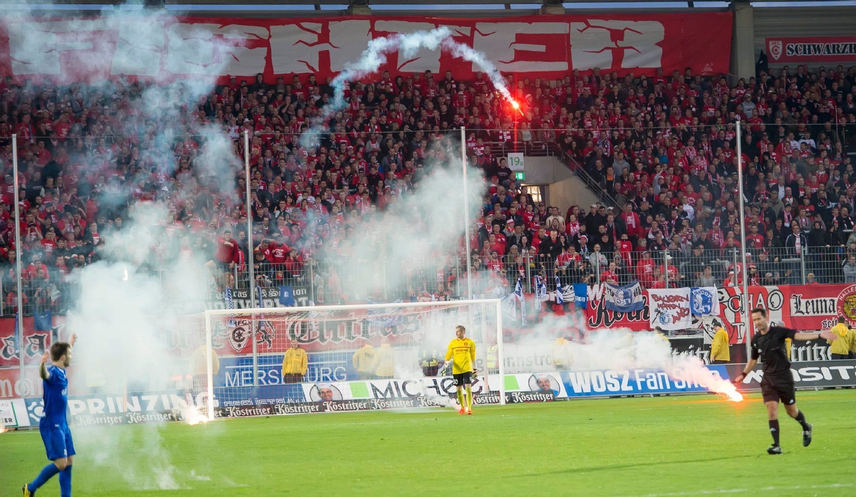 Schiedsrichter Patrick Kluge (re.) unterbricht das Spiel als Böller aus dem HFC-Fanblock aufs Spielfeld fliegen.