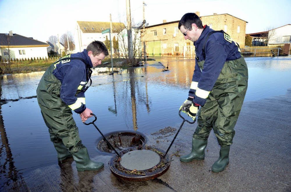 Roberto Lüth (l.) und Andy Schneider von der Freiwilligen Feuerwehr Baalberge öffnen den Gully, damit das Wasser besser ablaufen kann.