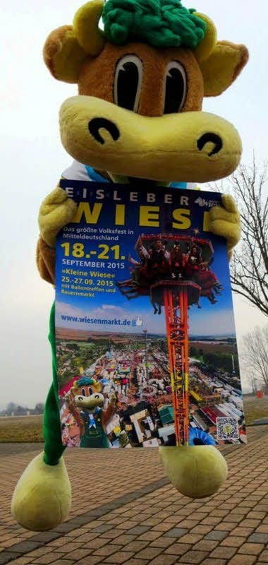 Maskottchen Wiesi schwebt mit dem neuen Plakat zur 494. Eisleber Wiese ein.