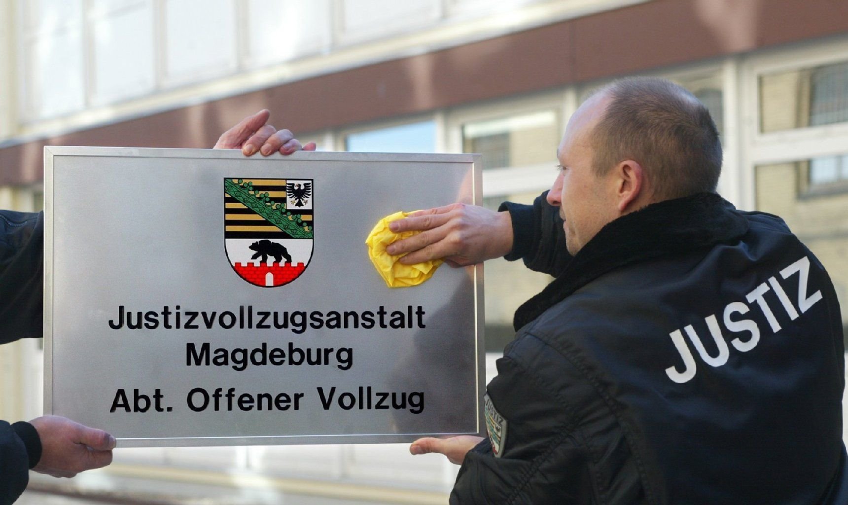 Justizvollzugsbeamte polieren ein Schild mit der Aufschrift: «Justizvollzugsanstalt Magdeburg Abt. Offener Vollzug».