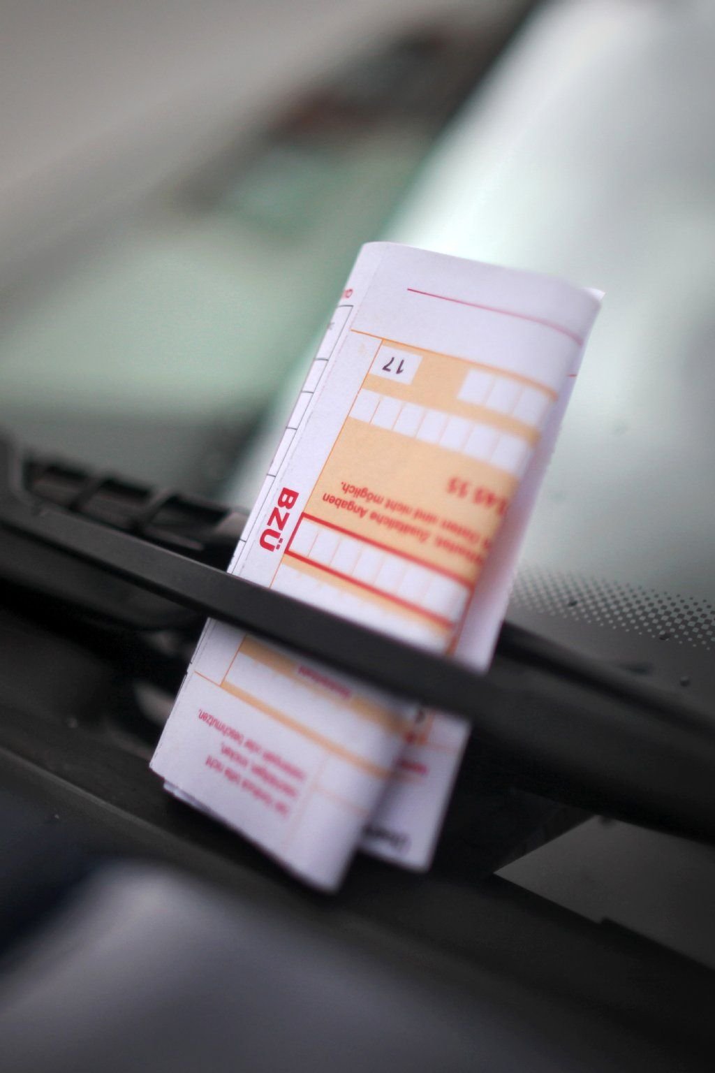 Ein Strafzettel (Knöllchen) steckt in einem Scheibenwischer eines geparkten Autos.