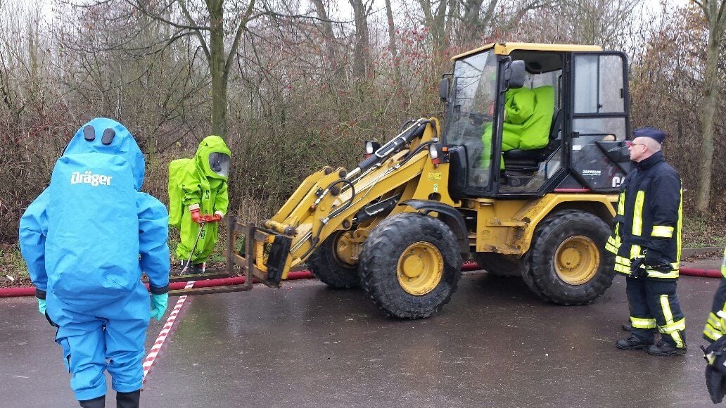 Feuerwehrleute unter Vollschutz transportieren das Nebelfass zum Ort der Entsorgung.