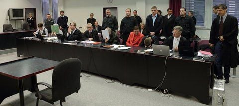 Anwälte, Dolmetscher und Justizangestellte stehen zwischen den Angeklagten beim Prozessauftakt im Landgericht in Dessau-Roßlau.