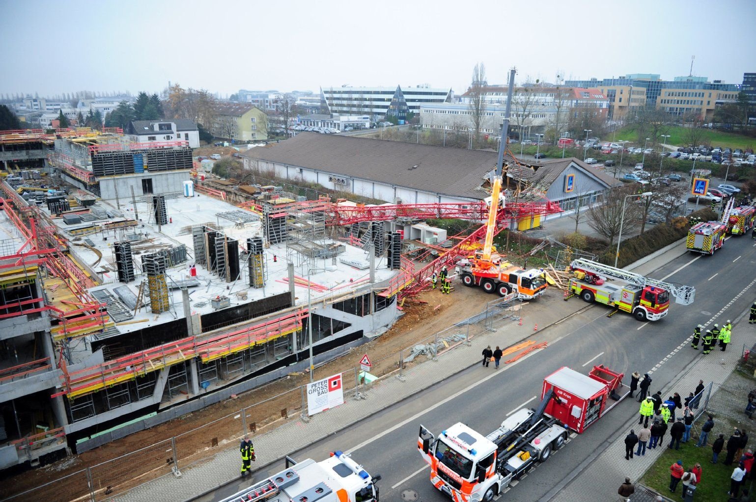 Helfer von Feuerwehr und THW stehen vor einem Supermarkt in Bad Homburg (Hessen), nachdem ein Kran auf das Gebäude gestürzt war.
