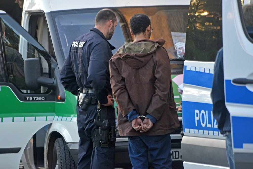 Ein Beamter bringt einen der Verdächtigen zum Polizeiwagen. Insgesamt elf Personen kamen zunächst in Gewahrsam.