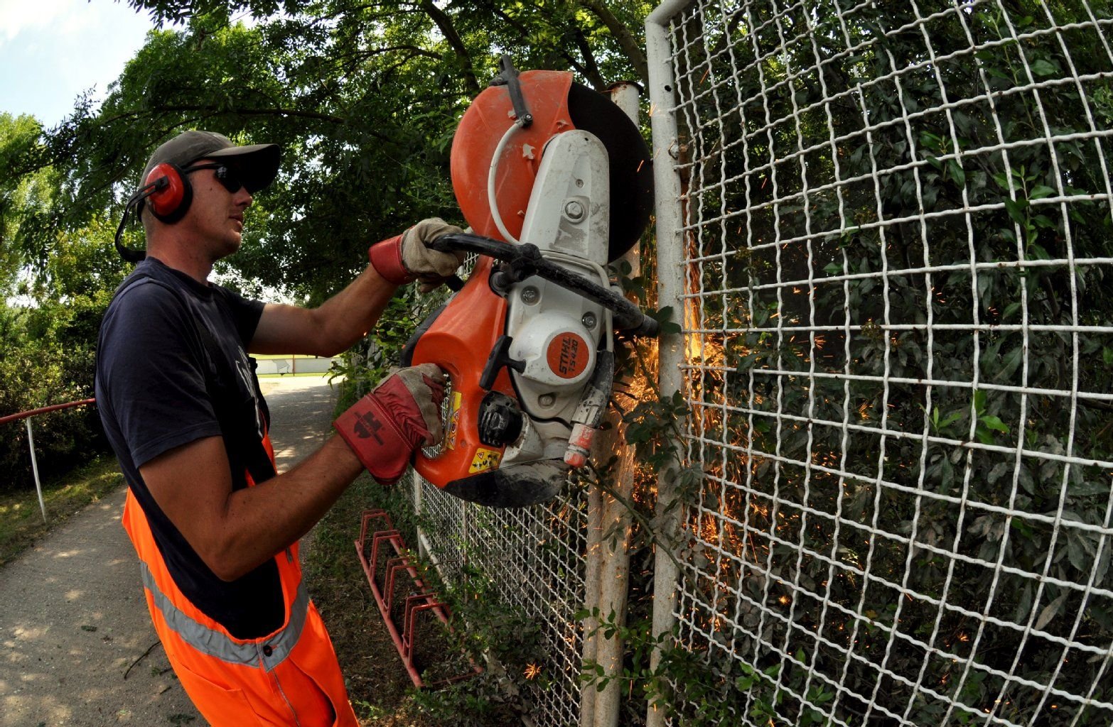 Arbeiter fällen die letzten Bäume und räumen am Gimritzer Damm in Halle-Neustadt auf. Ein Arbeiter trennt die Zäune zum angrenzenden Fußballplatz durch, um Platz für die Baumfällarbeiten zu machen.