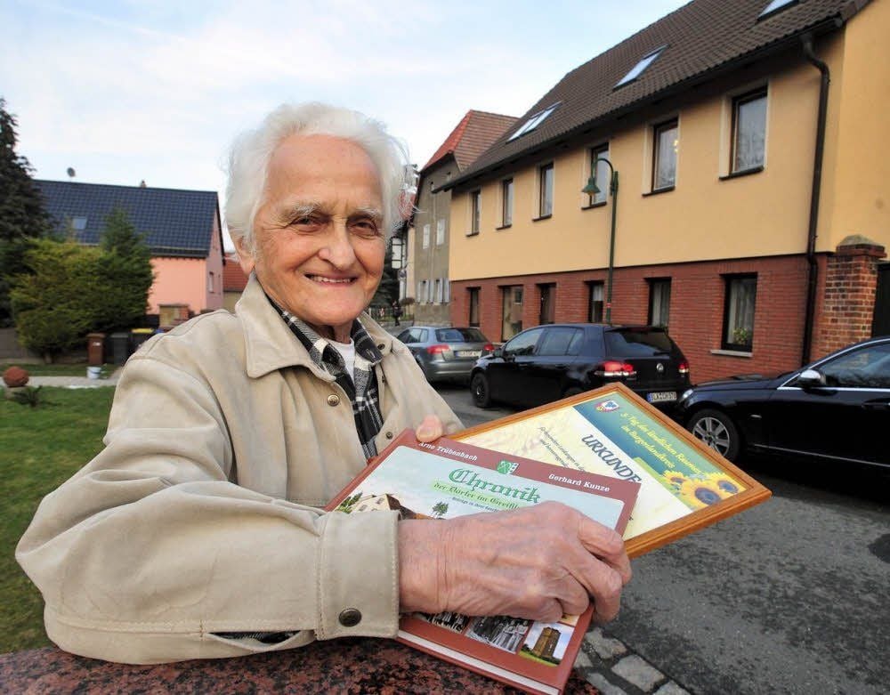 Gerhard Kunze steht vor seinem Geburtshaus in der Karl-Marx-Straße. Stolz zeigt er die Langendorfer Chronik und eine Urkunde, mit der sein Engagement für die Erforschung der Heimatgeschichte gewürdigt wird.