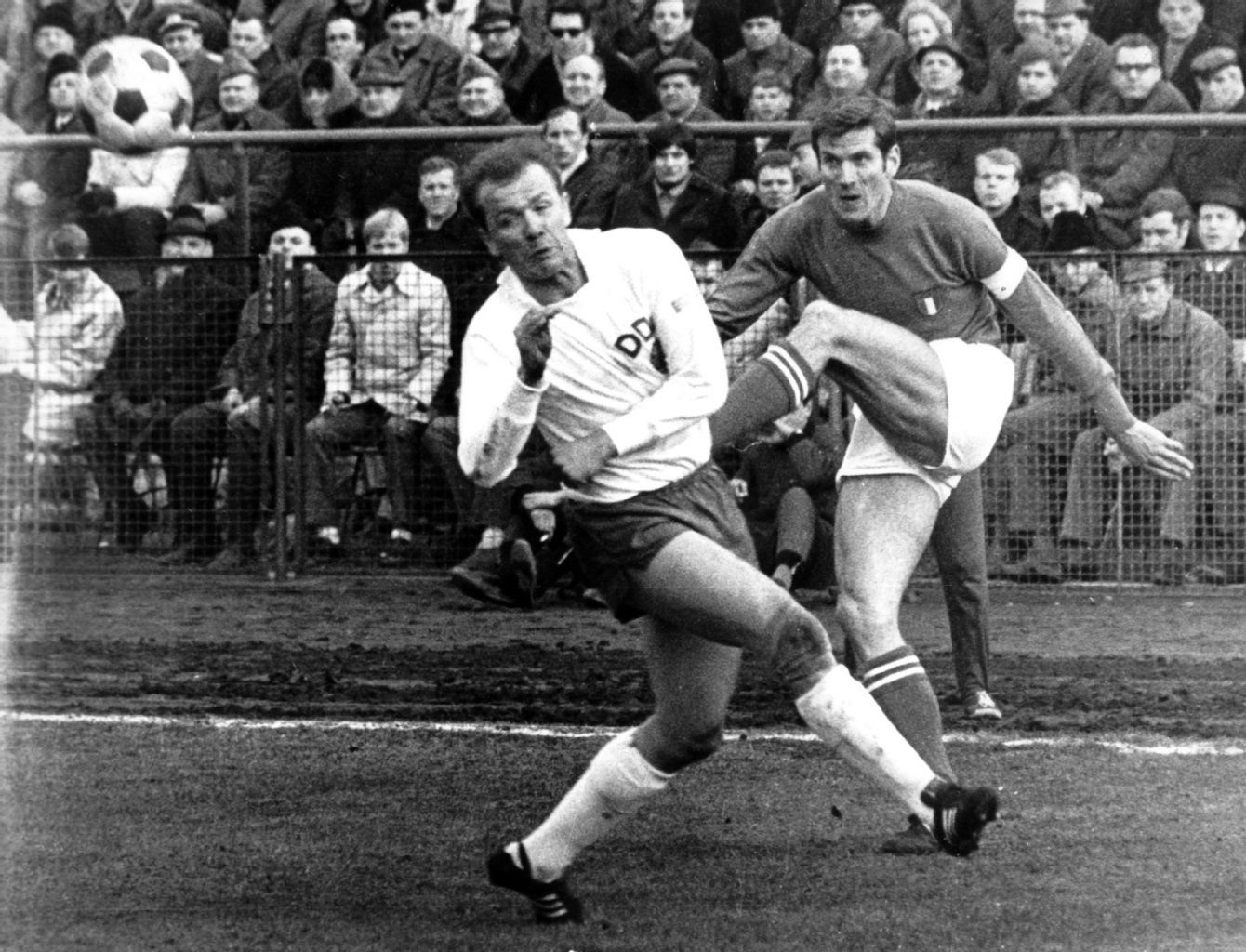 DDR-Verteidiger Klaus Urbanczyk (links) kann den Flankenball des italienischen Abwehrspielers und Kapitäns Giacinto Facchetti (dahinter) nicht abblocken, aufgenommen beim 2:2-Unentschieden im WM-Qualifikationsspiel der Fußball-Nationalmannschaft der DDR im Berliner Walter-Ulbricht-Stadion gegen Italien.