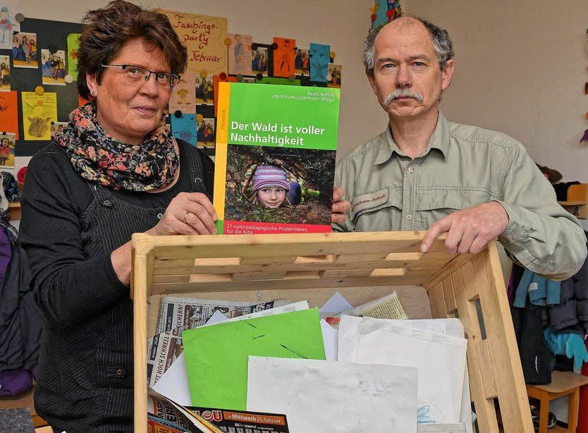 Erzieherin Ines Weinelt und Förster Jürgen Kristin präsentieren das Buch und eine Kiste, in denen die „Rasselbande“ Papier sammelt.
