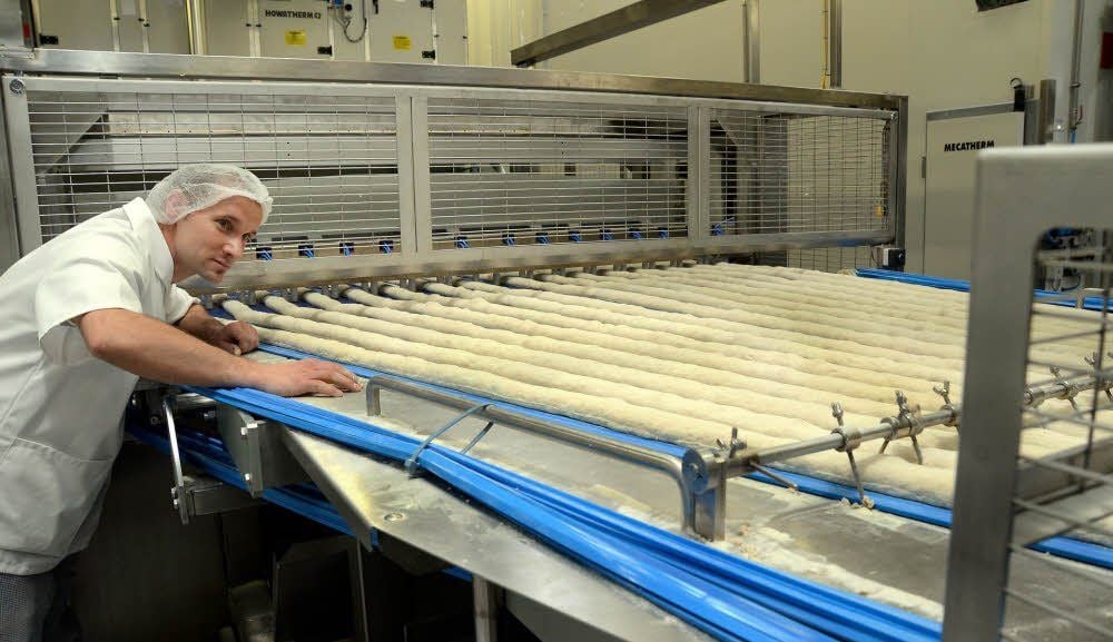 Mitarbeiter Karsten Metzsch beobachtet die Teigstreifen, die später als Steinofenbrötchen zu den Kunden gelangen.