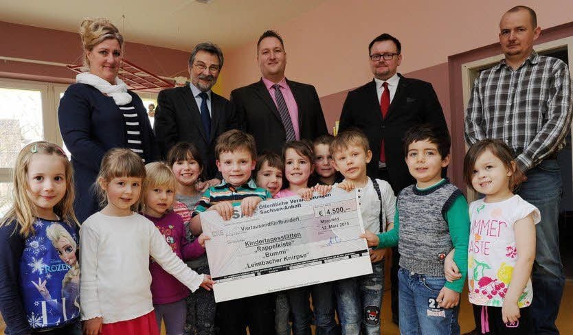 Andre Ulrich (2.v.r.) und Sebastian Ahlig (3.v.r.) von der Ösa übergaben in der Kita „Rappelkiste“ einen Scheck über 4.500 Euro für die Installation von Alarmanlagen in drei Kindereinrichtungen in der Stadt Mansfeld.